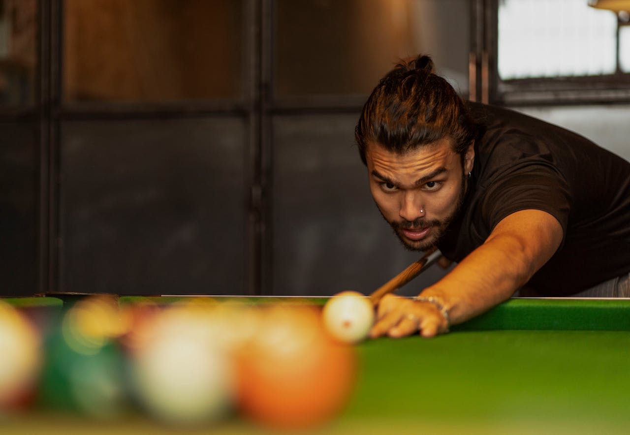 Man intensely focused on a billiard shot, showcasing skill and concentration in a cozy indoor setting.